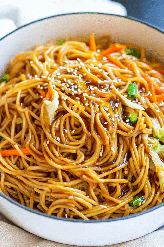 Glossy teriyaki noodles in a large pot with colorful vegetables, garnished with sesame seeds and green onions, showing the rich sauce coating