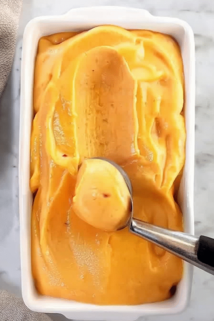 Refreshing peach sorbet in a bowl with fresh peach slices and mint – a light, fruity summer dessert